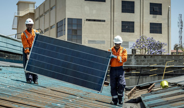 Zwei Afrikaner in Arbeitskleidung tragen ein Solarpanel über ein Hausdach.