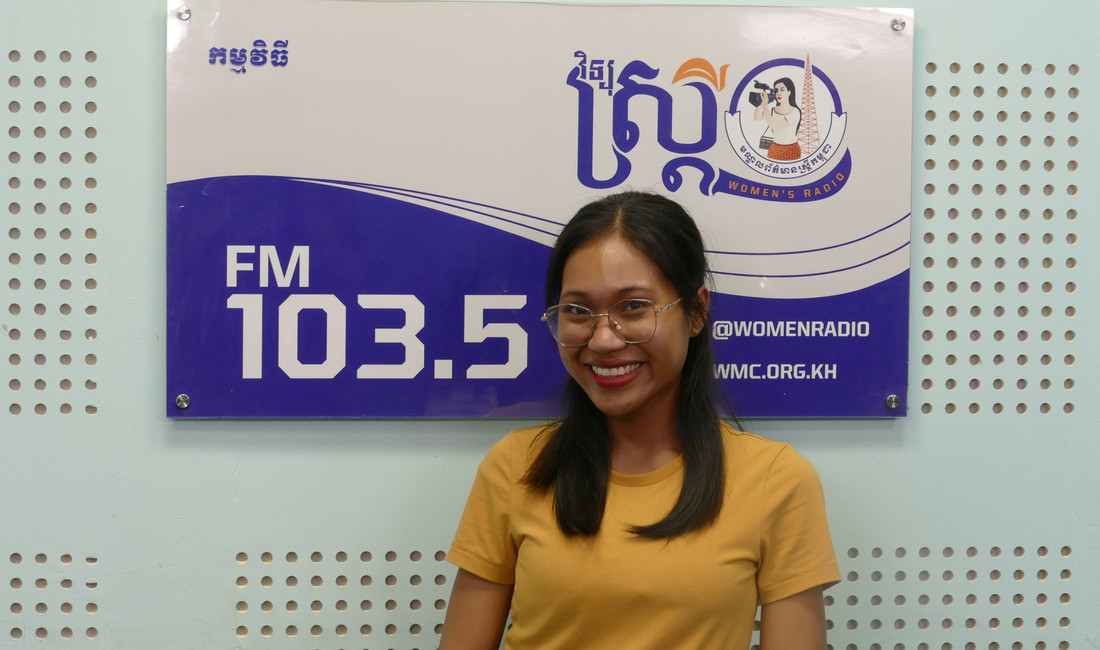 Die Moderatorin Noeun Sreynoch  im Studio des Women‘s Media Center of Cambodia. An der Wand hängt ein Schild mit der Aufschrift "FM 103.5". 