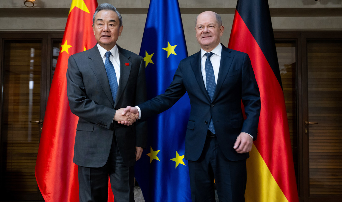 Bundeskanzler Olaf Scholz und der chinesische Außenminister stehen vor Fahnen und schütteln sich die Hände. 