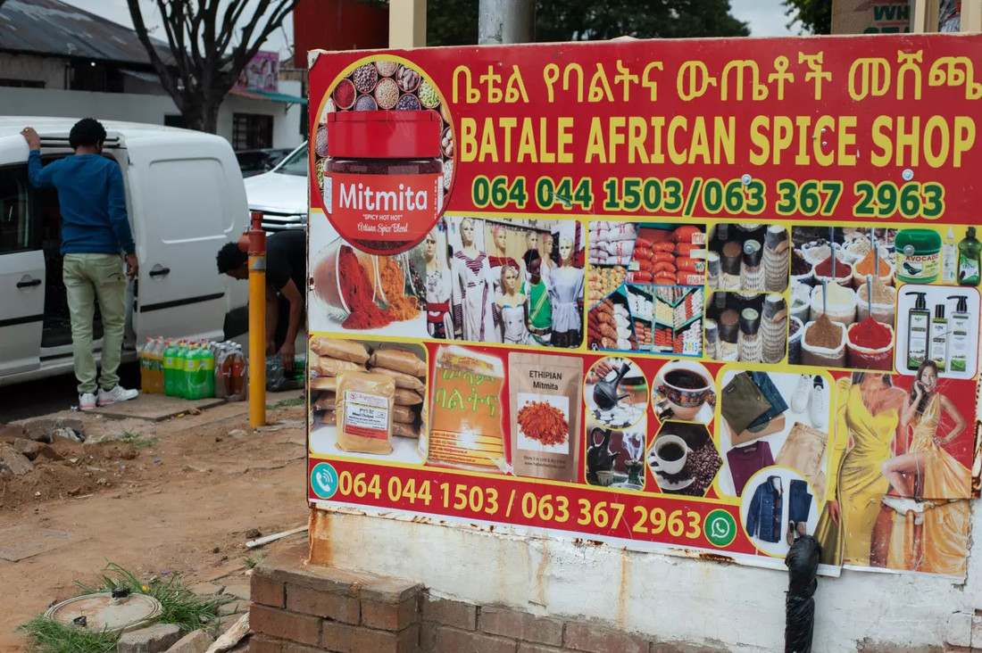 Zu sehen ist ein großes Schild eines afrikanischen Gewürzshops, seitlich steht ein Lieferwagen. 