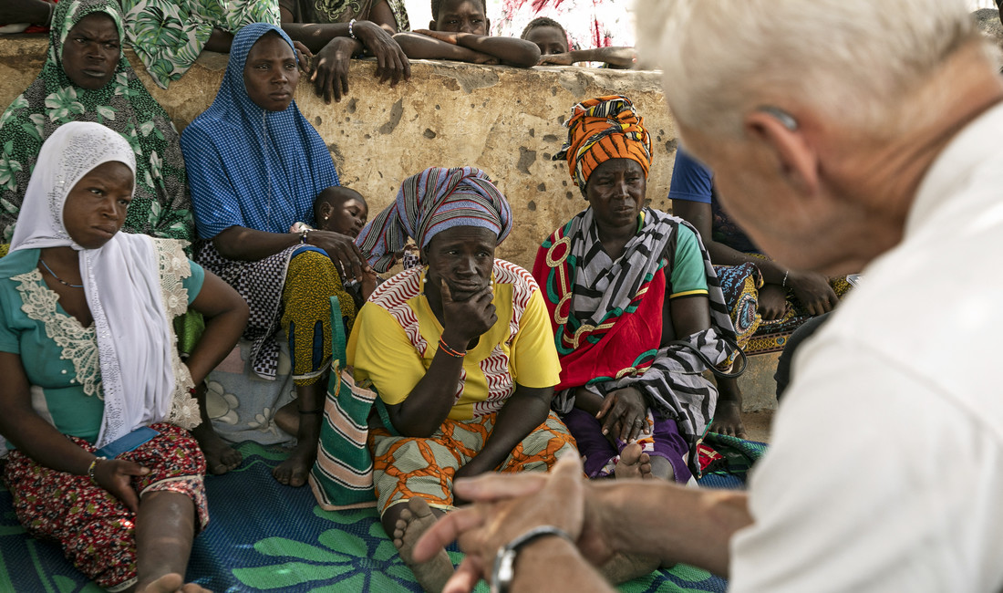 Sitzende Afrikanerinnen schauen einen Europäer an, der unscharf von hinten im Vordergrund erscheint.