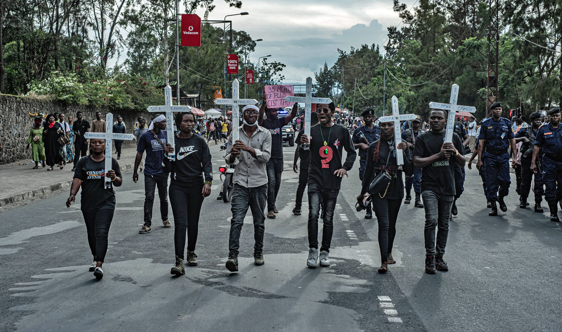 Mehrere Afrikaner laufen nebeneinander auf einer Straße. Jeder von ihnen hält ein großes weißes Kreuz mit einem Namen hoch. 