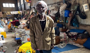 Ein Äthiopier steht in einer großen Fabrikhalle. Im Hintergrund sind Decken, Taschen und Habseligkeiten von anderen Flüchtlingen zu sehen. 