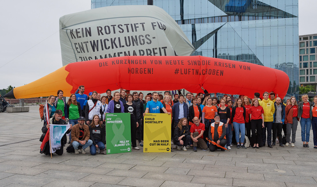 Mit einem zwölf Meter langen Rotstift hat ein Bündnis aus zivilgesellschaftlichen Organisationen Anfang Juni vor dem Berliner Hauptbahnhof gegen geplante Einsparungen bei Entwicklungspolitik und humanitärer Hilfe protestiert. Auf dem Foto sind Mitglieder von Save the Children, der Verband Entwicklungspolitik und Humanitäre Hilfe (VENRO), Oxfam, The ONE Campaign der Arbeiterwohlfahrt und andere. 