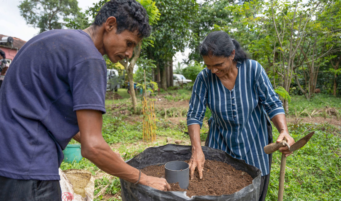 Ein dunkelhaariger Mann und eine dunkelhaarige Frau beugen sich über einen Plastiksack mit organischem Dünger. Im Hintergrund ein agrarisches Gelände in Sri Lanka.