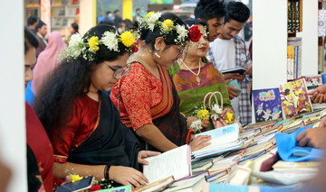 Frauen mit Blumen im Haar und traditioneller Kleidung stehen an einem Bücherstand in Bangladesch und lesen in Büchern. Im Hintergrund Männer, die ebenfalls in Bücher schauen.