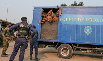 Männer in Polizei- und Militäruniformen bewachen einen blauen Gefangenentransport-Laster mit einer Tür, hinter der man zusammengepferchte kongolesische Männer sieht