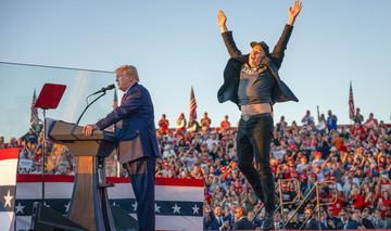 Donald Trump im Profil am Rednerpult bei einer Wahlveranstaltung in den USA, im Hintergrund eine Menschenmenge von Zuhörern, rechts neben ihm Elon Musk, der jubelnd die Arme in die Höhe reißt.